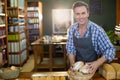 Middle-aged man wearing striped apron holding basket of loaves behind counter in bakery, copy space Royalty Free Stock Photo