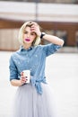 A portrait of a standing dreamy blonde girl with bright pink lips hoding a cup of cofee and holding one hand near her Royalty Free Stock Photo