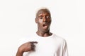 Portrait of startled, african-american blond guy looking surprised as pointing at himself with dropped jaw, standing Royalty Free Stock Photo