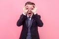 Portrait of startled surprised businessman in tuxedo looking at camera through fingers in ok gesture. indoor studio shot Royalty Free Stock Photo