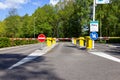 A portrait of a street closed by a barrier bar with some traffic signs in front of them. The automatic gate system provides some