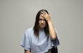 Portrait of stressed beautiful brunette woman in a blue t-shirt holding her head with hands having headache over grey