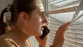 Portrait of stressed and scared woman loooking through window blinds on the street after seeing a crime Royalty Free Stock Photo