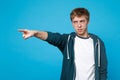 Portrait of strict angry young man in casual clothes pointing index finger aside isolated on blue background in studio Royalty Free Stock Photo
