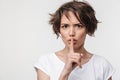 Portrait of strict woman with short brown hair in basic t-shirt holding index finger on lips Royalty Free Stock Photo