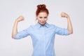 Strong confident ginger woman raising arms showing biceps, female strength and feminism.