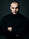 Portrait of strong man, athlete, sportsman in black sweater turtleneck standing with arms crossed at chest