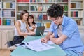 Portrait of student guy at desk inside college library, female student together with teacher preparing for exam. Royalty Free Stock Photo