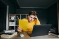 Portrait of a student studying in quarantine remotely, sitting at home at a table with books, holding a notebook and looking at a Royalty Free Stock Photo