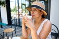 Portrait: Stunning mysterious Latin American woman, in straw hat and elegant summer dress enjoying coffee break outdoors