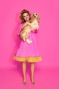 Portrait of stunning, young, woman wearing like sweet doll over pink studio background. Lady with cute dog Royalty Free Stock Photo