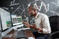 See the difference. Portrait of stylish african businessman, trader sitting by desk in front of multiple monitors. He is