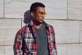 Portrait of stylish african man wearing sunglasses, red plaid shirt, guy looking away posing on city street Royalty Free Stock Photo