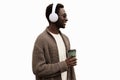 Portrait of stylish african man in wireless headphones listening to music with coffee cup looking away wearing brown knitted Royalty Free Stock Photo