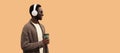 Portrait of stylish african man in wireless headphones listening to music with coffee cup looking away wearing knitted cardigan Royalty Free Stock Photo