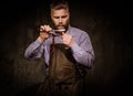 Portrait of stylish barber with beard and professional tools on a dark background.