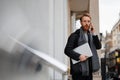 Portrait of a stylish bearded business man with a laptop in his hands talking on the smartphone. Royalty Free Stock Photo