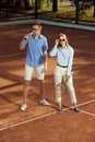 Full-length portrait of stylish, beautiful young man and woman in casual clothes posing on opendoor tennis court on warm Royalty Free Stock Photo