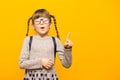 Portrait of stylish child girl pointed finger up. Little child in glasses has idea. Kid isolated on yellow background