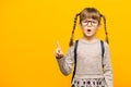 Portrait of stylish child girl pointed finger up. Little child in glasses has idea. Kid isolated on yellow background