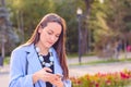 Portrait of stylish girl in a blue coat and beads, reading emails on a smartphone in a Park backlit.