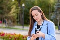 Portrait of stylish girl in a blue coat and beads, reading emails on a smartphone in a Park backlit.