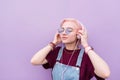 Portrait of a stylish girl who listens to music in pink headphones on the background of a purple wall Royalty Free Stock Photo