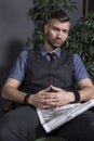 Portrait of stylish handsome man in chair with newspaper. Attractive brutal confident businessman