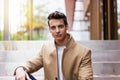 Portrait of stylish handsome young man with coat sitting outdoors Royalty Free Stock Photo