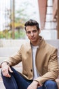 Portrait of stylish handsome young man with coat sitting outdoors Royalty Free Stock Photo