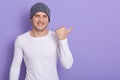 Portrait of stylish handsome young man osing isolated over lilac background. Male smiling and points aside, wears white casual