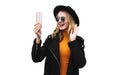 Portrait stylish happy laughing young woman having video call or taking selfie by phone wearing a black coat, round hat Royalty Free Stock Photo