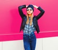 portrait stylish happy smiling woman in rock black style jacket, hat posing on city street over colorful pink wall Royalty Free Stock Photo