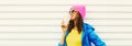 Portrait of stylish happy smiling young woman with cup of coffee wearing colorful pink hat, blue jacket on white background Royalty Free Stock Photo