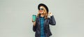 Portrait of stylish happy smiling young woman holds cup of coffee wearing round hat and rock style black leather jacket posing on Royalty Free Stock Photo