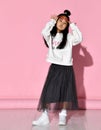 Portrait of a stylish Korean girl wearing a white sweater, tulle skirt, sneakers and red glasses.