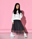 Portrait of a stylish Korean girl wearing a white sweater, tulle skirt, sneakers and red glasses.