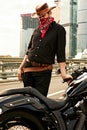 Portrait of stylish male dressed in a black leather jacket and bandana sitting on his custom-made retro motorcycle Royalty Free Stock Photo