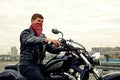 Portrait of stylish male dressed in a black leather jacket and bandana sitting on his custom-made retro motorcycle Royalty Free Stock Photo