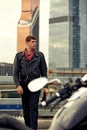 Portrait of stylish male dressed in a black leather jacket and bandana sitting on his custom-made retro motorcycle