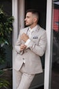 Portrait of stylish man standing on terrace near the window and posing to photographer. Handsome grown in light colour Royalty Free Stock Photo