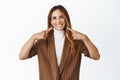 Portrait of stylish middle aged woman pointing fingers at her perfect white smile, showing dental clinic work, standing Royalty Free Stock Photo