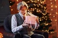 Portrait of stylish senior with grey hair and beard is in decorated christmas room with gift box