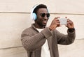 Portrait stylish smiling african man taking selfie picture by smartphone in wireless headphones listening to music Royalty Free Stock Photo