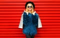 Portrait stylish smiling woman with shopping bags wearing blue faux fur coat, round hat and sunglasses posing over red wall