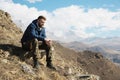 A portrait of a stylish smirk bearded hipster sitting on a rock against the backdrop of epic rocks and contemplating