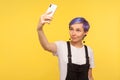 Portrait of stylish trendy hipster girl holding smartphone and taking selfie photo, making video call. studio shot Royalty Free Stock Photo