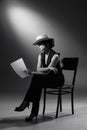 Portrait of stylish woman in classic black suit and straw hat, posing, sitting on chair and reading. Black and white Royalty Free Stock Photo