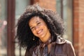 Portrait of stylish young African American woman smiling and looking at camera. Brunette with curly hair in brown