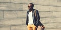 Portrait of stylish young african man model posing wearing black rock leather jacket with bag on city street background Royalty Free Stock Photo